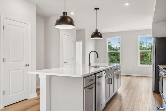 kitchen with decorative light fixtures, a center island with sink, light hardwood / wood-style flooring, and sink