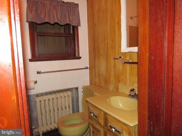 bathroom featuring radiator heating unit, vanity, toilet, and wood walls