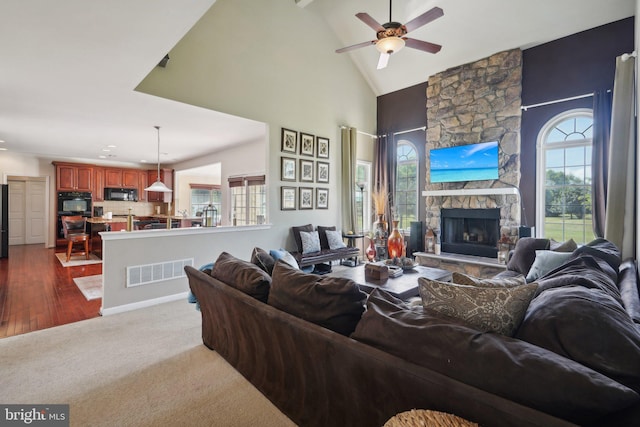 living room with high vaulted ceiling, a stone fireplace, a wealth of natural light, and ceiling fan