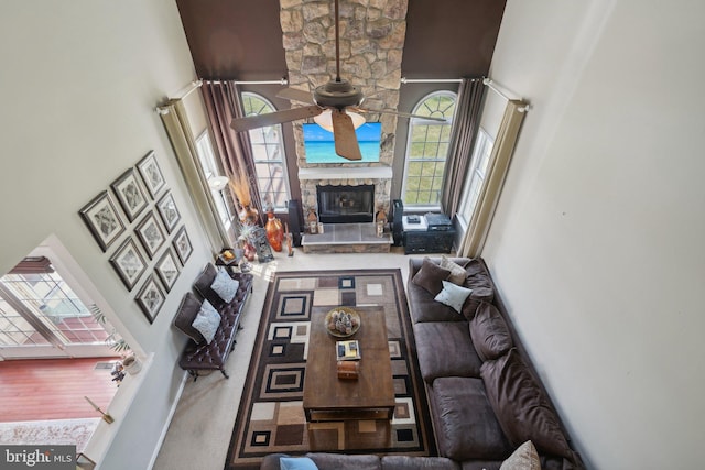 living room with a high ceiling, a stone fireplace, and ceiling fan