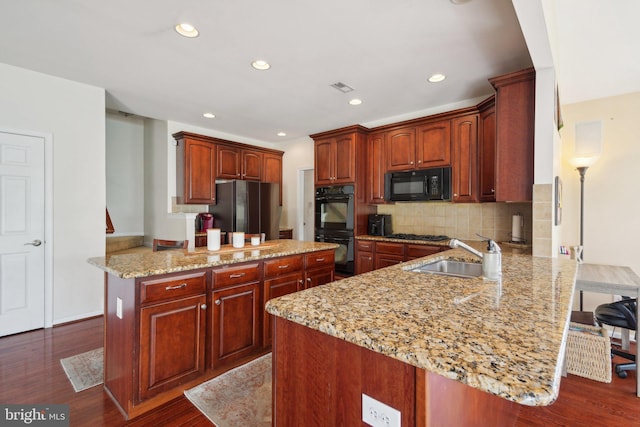 kitchen with a breakfast bar, black appliances, sink, dark hardwood / wood-style flooring, and kitchen peninsula