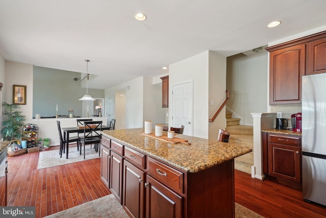 kitchen featuring dark hardwood / wood-style flooring, light stone counters, decorative light fixtures, a center island, and stainless steel refrigerator