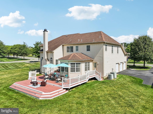 rear view of property featuring a lawn, a wooden deck, central AC unit, and a garage