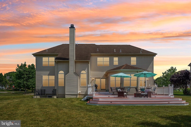 back house at dusk with a yard and a deck