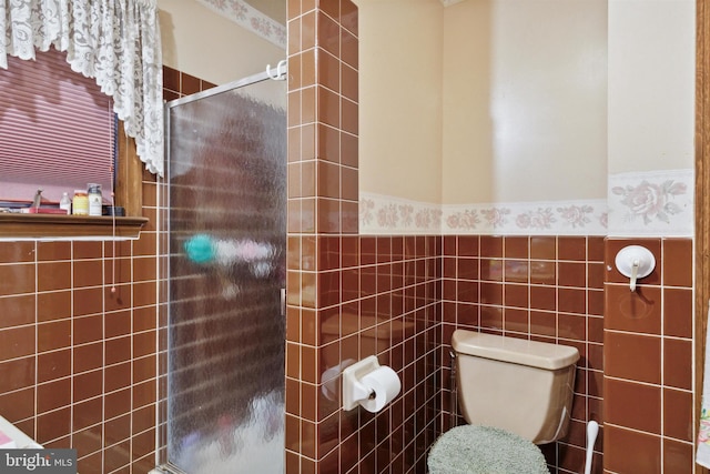 bathroom featuring toilet, a shower with shower door, and tile walls