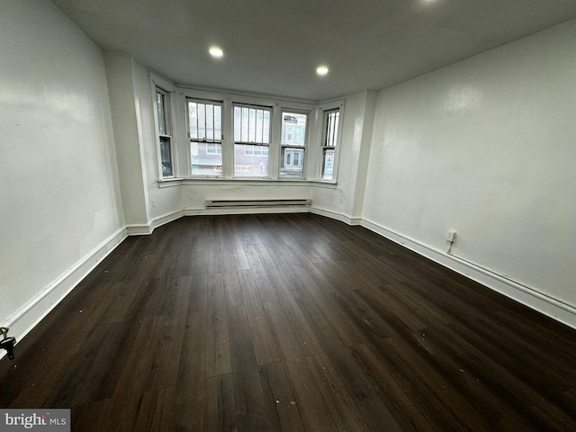 unfurnished room featuring dark hardwood / wood-style flooring and a baseboard heating unit