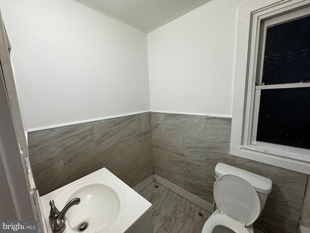 bathroom featuring toilet, tile walls, and sink