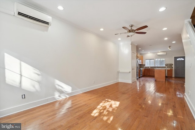 unfurnished living room featuring light hardwood / wood-style flooring, an AC wall unit, ceiling fan, and sink