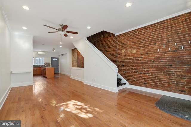 unfurnished living room with ceiling fan, sink, light hardwood / wood-style flooring, brick wall, and crown molding