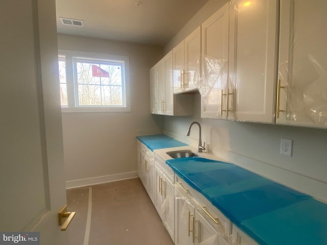 kitchen featuring visible vents, white cabinetry, and a sink