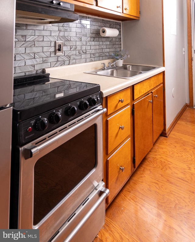 kitchen with tasteful backsplash, gas range, sink, and light hardwood / wood-style floors