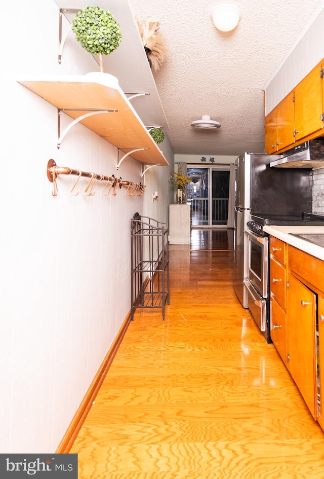 kitchen featuring wood walls, a textured ceiling, stainless steel range with gas stovetop, and light hardwood / wood-style flooring