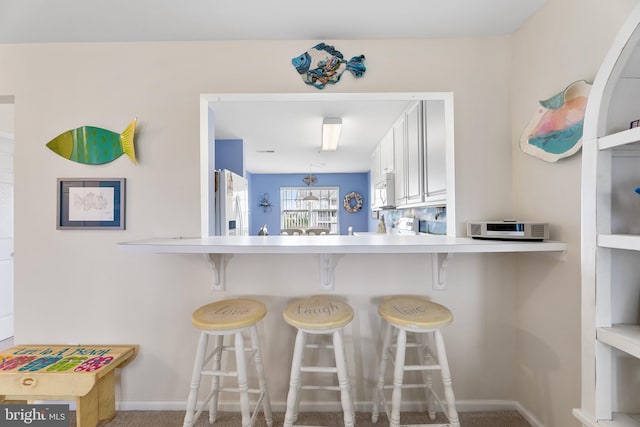 kitchen featuring white cabinetry, a kitchen breakfast bar, kitchen peninsula, white appliances, and carpet