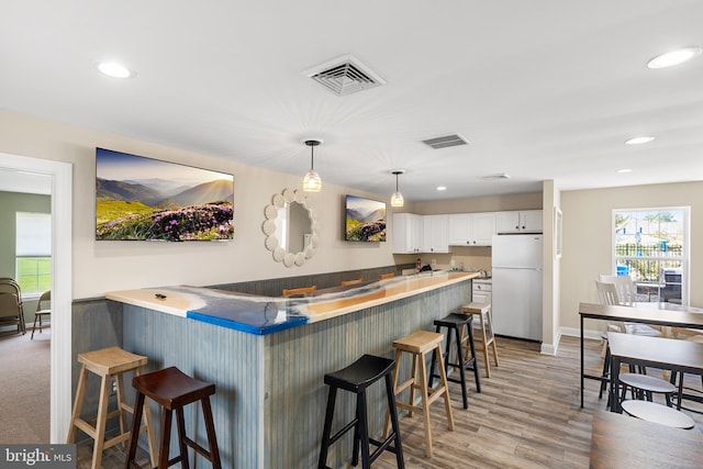 kitchen featuring white cabinetry, a kitchen breakfast bar, kitchen peninsula, white fridge, and light wood-type flooring