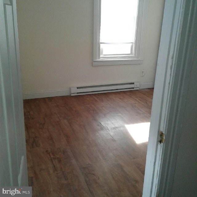 empty room featuring dark hardwood / wood-style flooring and a baseboard heating unit