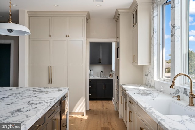 kitchen featuring light stone counters, sink, decorative light fixtures, and light wood-type flooring