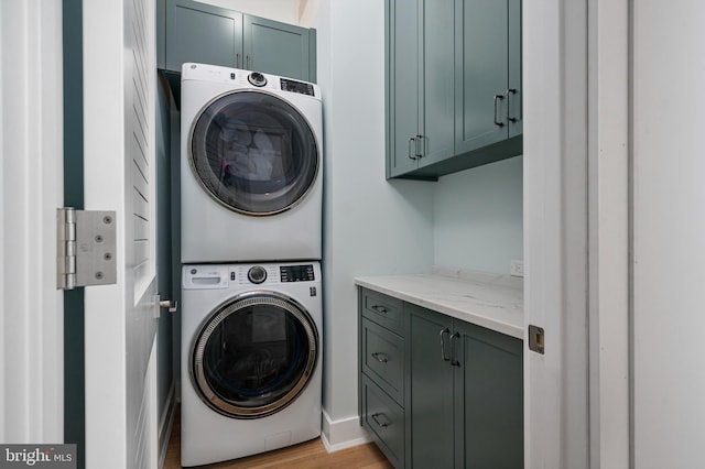 laundry room featuring cabinets, light wood-type flooring, and stacked washing maching and dryer