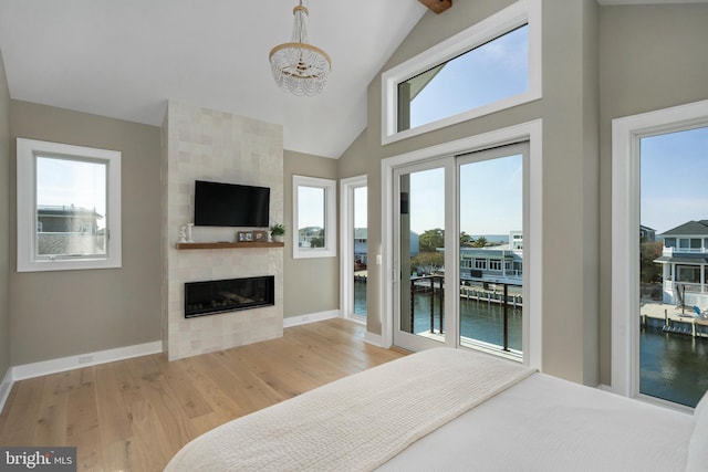 bedroom with access to exterior, a large fireplace, high vaulted ceiling, an inviting chandelier, and light hardwood / wood-style floors