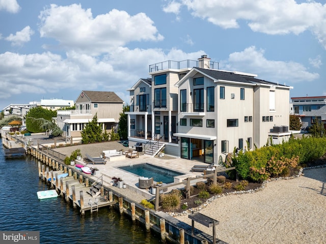 rear view of house featuring a balcony, a water view, a patio, and a swimming pool