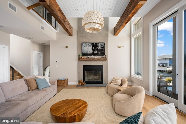 living room with beamed ceiling, light hardwood / wood-style floors, a fireplace, and an inviting chandelier