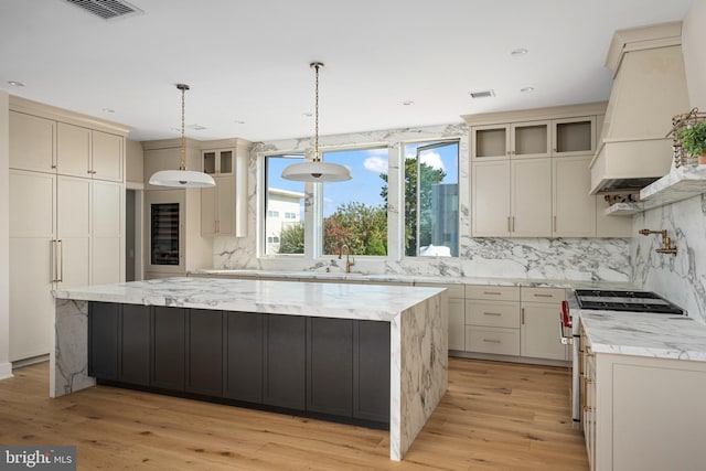 kitchen with pendant lighting, a spacious island, custom range hood, and light hardwood / wood-style flooring