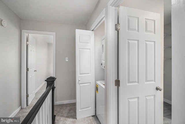 corridor with light colored carpet and stacked washer and clothes dryer