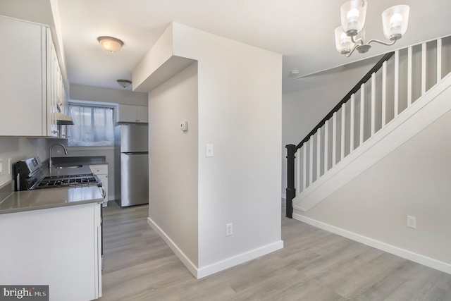 kitchen with sink, stainless steel appliances, decorative light fixtures, white cabinets, and light wood-type flooring