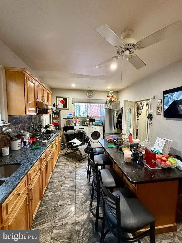 kitchen featuring ceiling fan, stainless steel appliances, tasteful backsplash, washing machine and dryer, and a breakfast bar