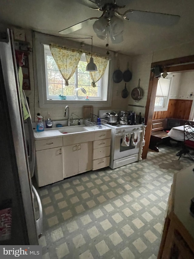 kitchen featuring stainless steel fridge, white range with gas cooktop, sink, decorative light fixtures, and white cabinets