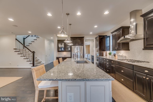 kitchen with appliances with stainless steel finishes, a large island with sink, a kitchen breakfast bar, and wall chimney range hood