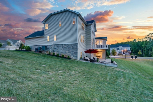 property exterior at dusk featuring central AC unit, a balcony, a yard, and a patio