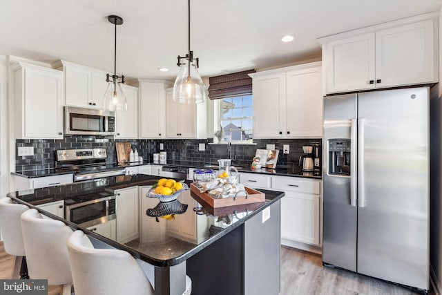 kitchen with appliances with stainless steel finishes, light wood-type flooring, a breakfast bar, white cabinets, and hanging light fixtures