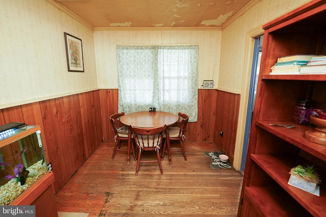 dining space with wood walls, wood-type flooring, and ornamental molding