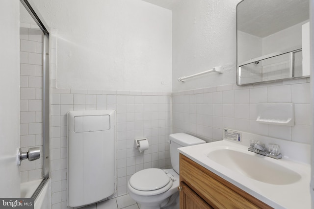 full bathroom featuring tile patterned floors, bath / shower combo with glass door, toilet, vanity, and tile walls