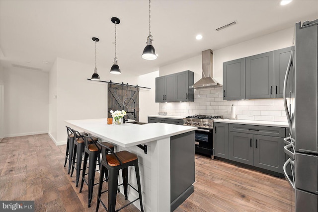 kitchen with pendant lighting, a center island with sink, wall chimney exhaust hood, a barn door, and appliances with stainless steel finishes