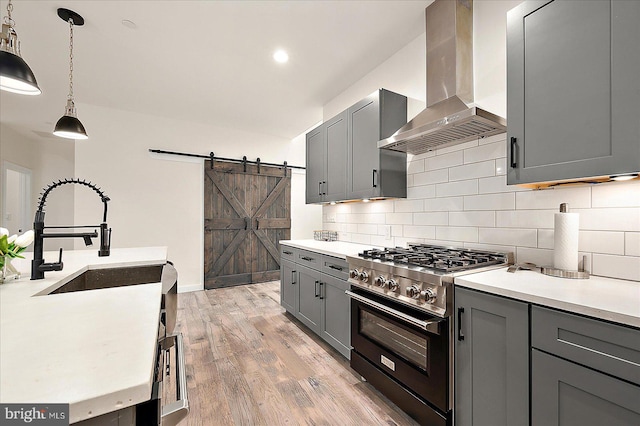 kitchen featuring light hardwood / wood-style flooring, wall chimney exhaust hood, gray cabinets, a barn door, and gas stove