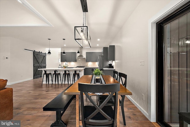 dining space featuring a barn door, dark wood-type flooring, and an inviting chandelier