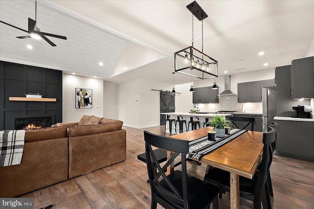 dining area with light wood-type flooring, a large fireplace, vaulted ceiling, and ceiling fan