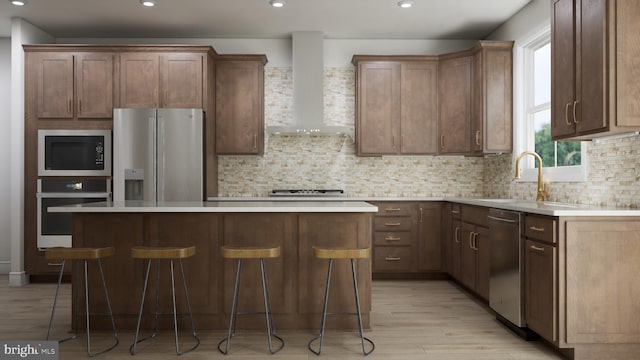 kitchen with a kitchen breakfast bar, wall chimney range hood, sink, a kitchen island, and stainless steel appliances