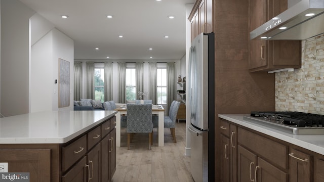 kitchen featuring stainless steel appliances, range hood, decorative backsplash, a kitchen island, and light wood-type flooring