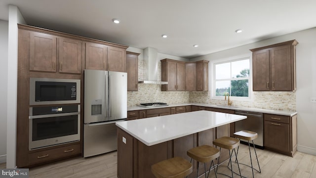 kitchen featuring a center island, wall chimney range hood, decorative backsplash, appliances with stainless steel finishes, and light hardwood / wood-style floors