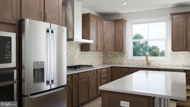 kitchen with backsplash, stainless steel appliances, wall chimney range hood, sink, and a center island