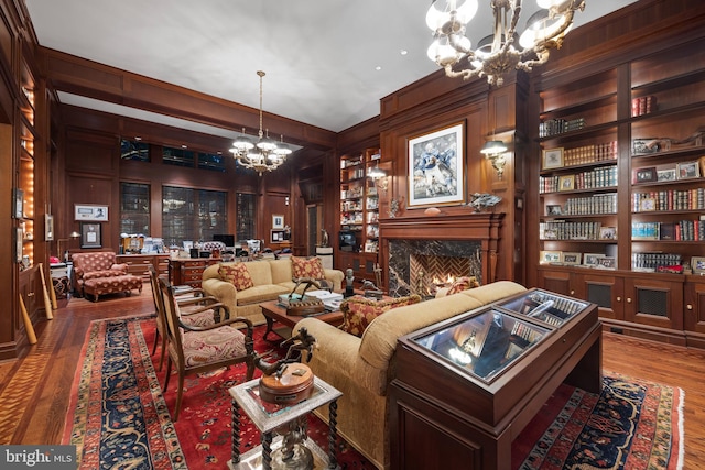 living room featuring a fireplace, wood-type flooring, an inviting chandelier, and built in shelves