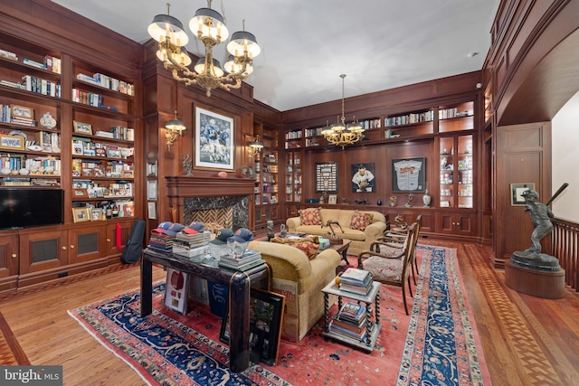 living room with a fireplace, built in shelves, wooden walls, light hardwood / wood-style flooring, and a chandelier