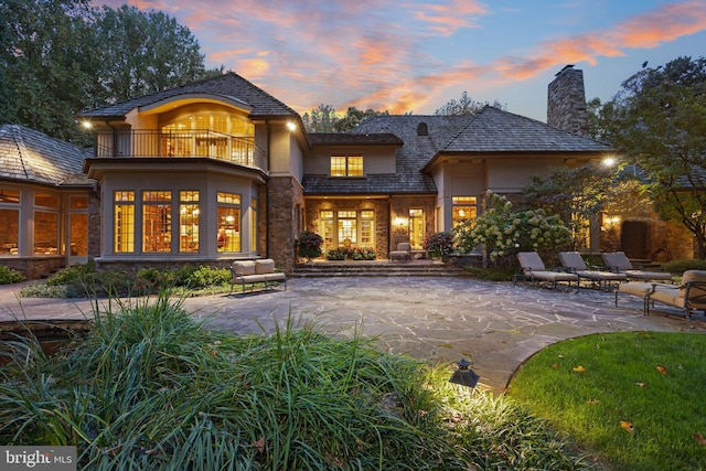 back house at dusk with a balcony and a patio area