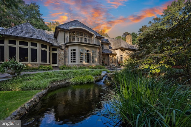 back house at dusk featuring a garden pond and a balcony