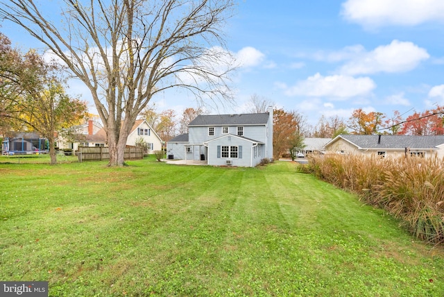 rear view of property with a trampoline and a yard