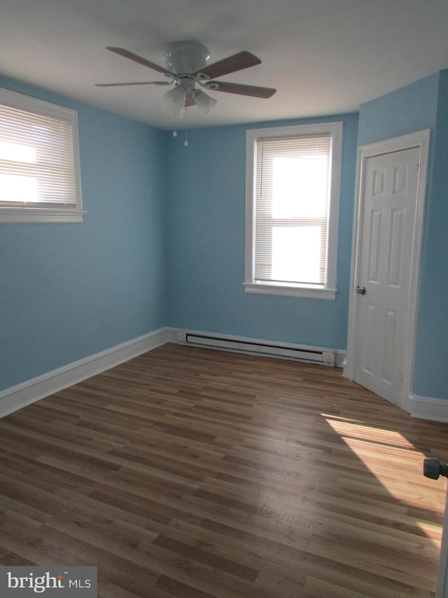 spare room with a baseboard heating unit, dark wood finished floors, a ceiling fan, and baseboards