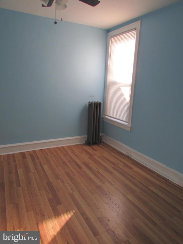 empty room with baseboards, ceiling fan, dark wood-style flooring, and radiator