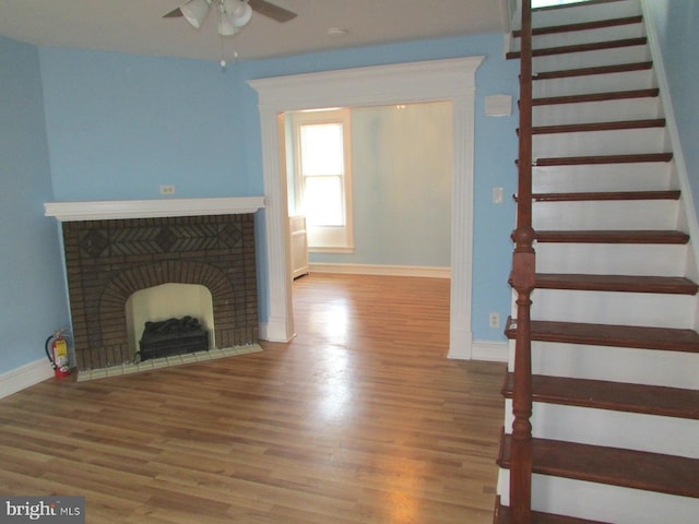 unfurnished living room featuring baseboards, ceiling fan, stairway, wood finished floors, and a fireplace